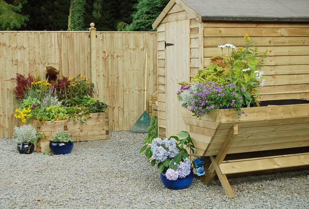 a gravel-floored garden with a wooden fence, wooden shed and wooden planters