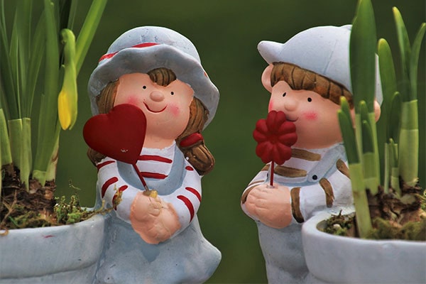 models of a boy and girl, holding a heart and flower, stood next to plant pots