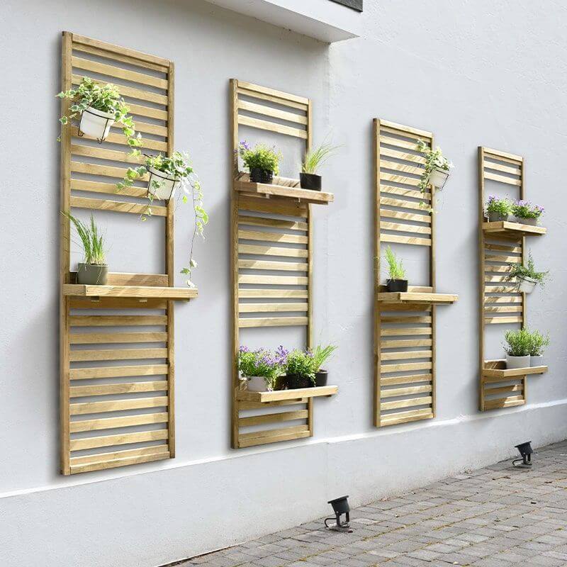 4 slatted wall planters, populated with 15 potted plants on shelves and hooked on the slats, attached to a plain white wall with 2 spotlights pointed up at the 2nd and 4th planters