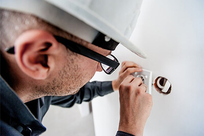 a man wearing black-rimmed glasses and a white hard hat inspects a switch in his hands