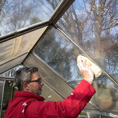 a man cleaning a greenhouse's glazing
