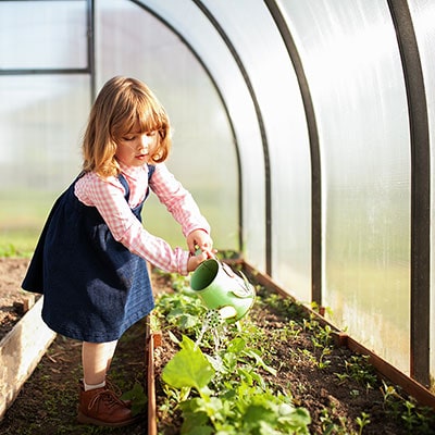 a child watering plants in a greenhouse