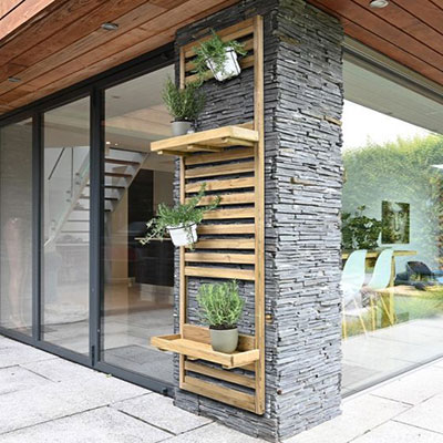 a slatted tall wall planter with 2 shelves and 4 potted plants