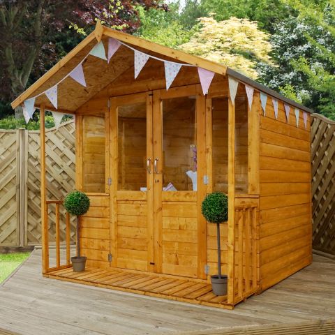 The 7x7 Windsor Traditional Wooden Summer House, situated on garden decking, with 2 plants on the veranda and triangular flags pinned to the eaves.