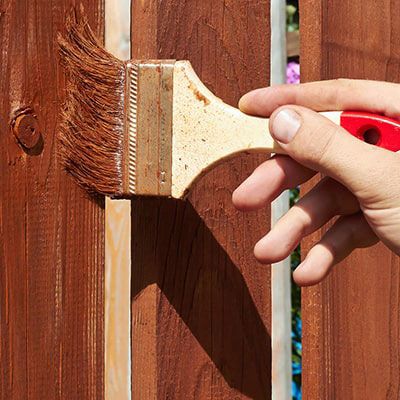 a hand holding a brush, applying wood preservative to a fence