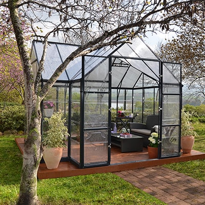 Palram Victory Greenhouse and Orangery Sun Lounge with garden furniture inside in a garden setting
