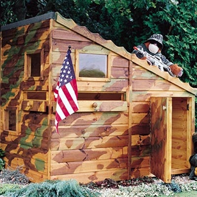 a camouflaged wooden playhouse, like an army base, with an American flag and a soldier looking out from the pent roof