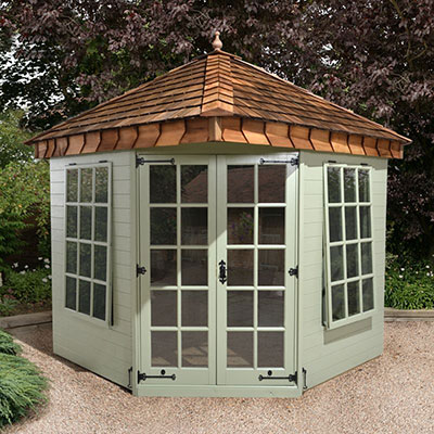 A green, hexagonal summer house with a brown shingle roof