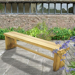 The Forest Double Sleeper Wooden Garden Bench 6x1, positioned on grass at the side of a path, with yellow and orange flowers in the background.