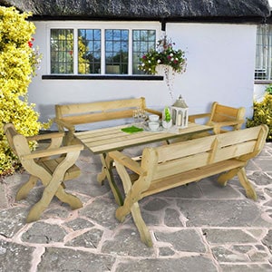 The Forest Grizedale 8 Seater Wooden Garden Table and Chairs Dining Set, situated on a patio, at the back of a white cottage with a thatched roof.