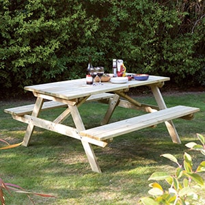 The Rowlinson 4ft Wooden Garden Picnic Bench, situated on a lawn and with condiments on the table.