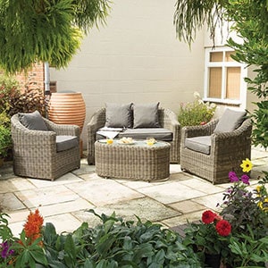 The Rowlinson Bunbury Rattan Garden Patio Furniture Set, including a sofa, 2 chairs and a table, situated on a patio.