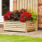 The Rowlinson Garden Creations Wooden Rectangular Planter 3x1, full of red and green flowers, situated on a patio.