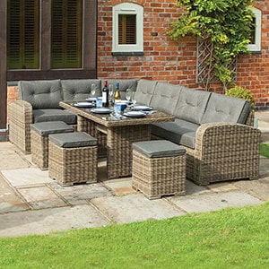 The Rowlinson Thornbury Corner Rattan Garden Table and Chairs Dining Set, situated on a patio, with plates, glasses and bottles of wine on the table.