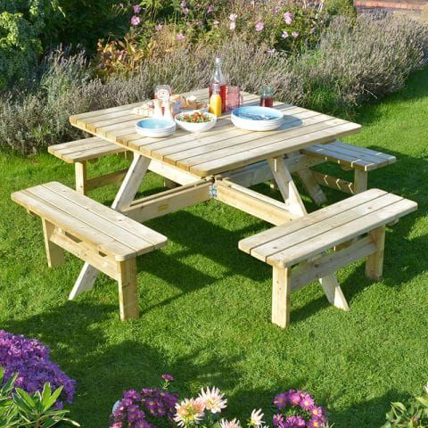 The Rowlinson Square Wooden Garden Picnic Table, nibbles and condiments on the table, which is situated on a lawn.