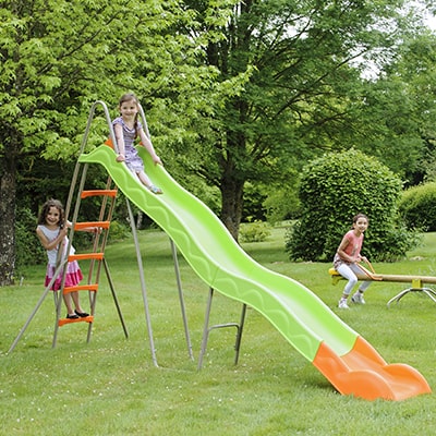 children playing on a green and orange, long, wavy slide