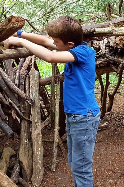 boy building a den in the woods with branches