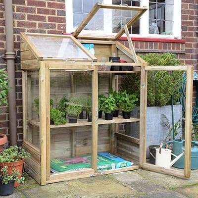 a small wooden-framed greenhouse, positioned against a wall