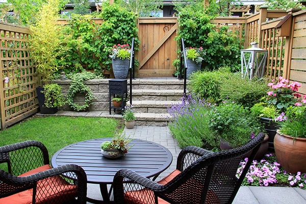 a small enclosed garden with table, chairs, planters and a raised area