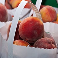 Lots of ripe peaches in white paper bags.
